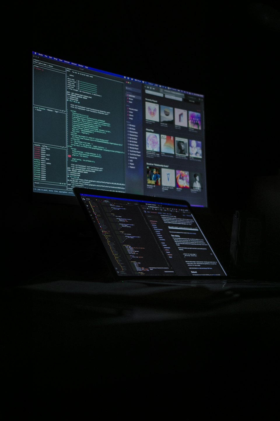 Laptop und Monitor mit komplexem Code in einem dunklen Raum.